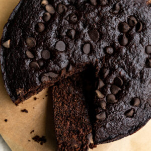 A chocolate banana cake with a slice cut out on brown parchment paper.
