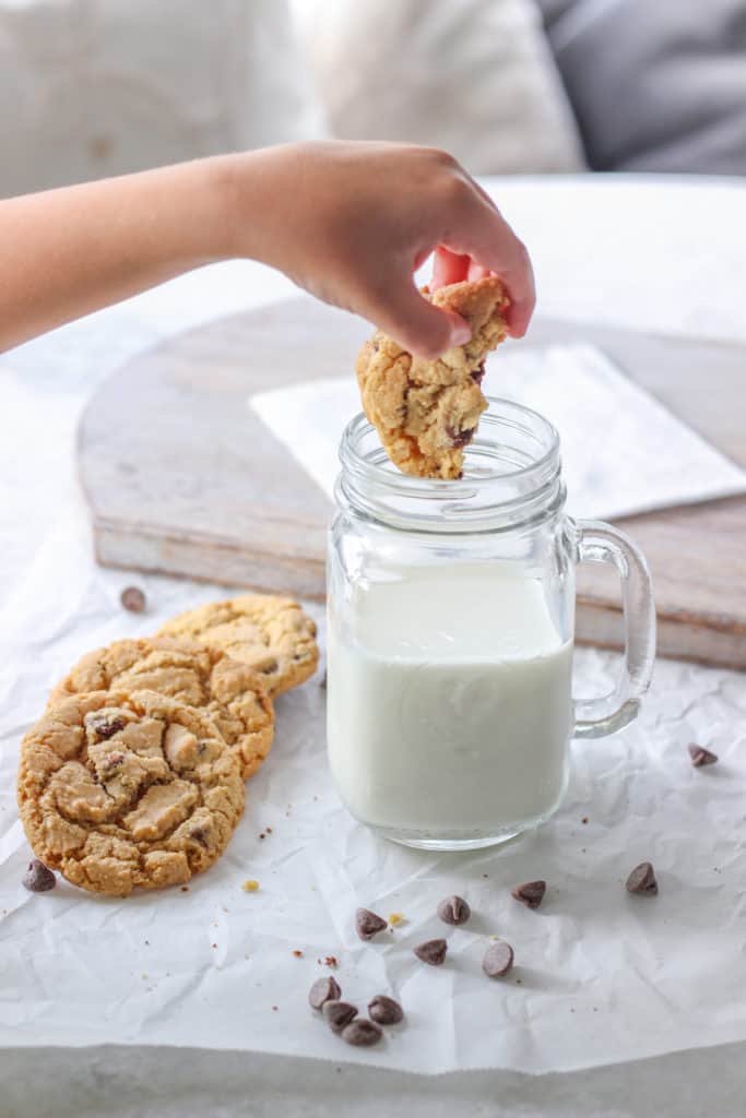 dunking half of a chewy chocolate chip cookie into a large glass of milk