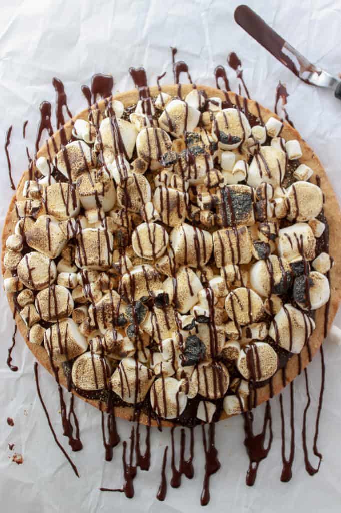 One giant graham cracker infused sugar cookie, topped with silky smooth chocolate ganache, and then loaded with marshmallows just waiting to be torched up. #smores #cookiecake #giantcookie Frostingandfettuccine.com