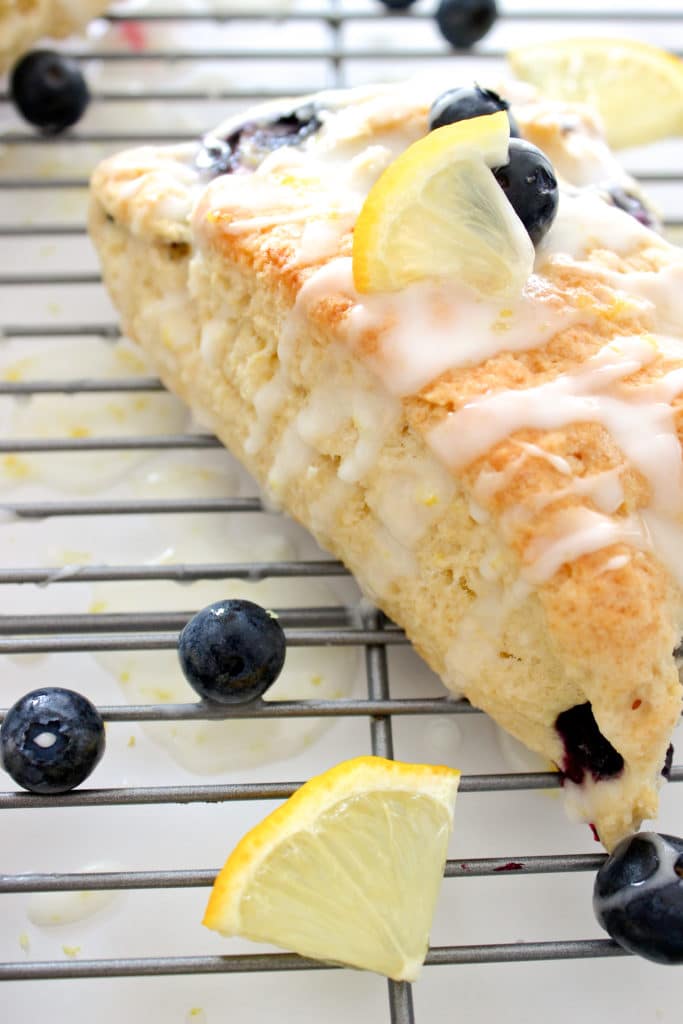 Blueberry lemon scones with lemon glaze dripping down the sides sitting on a cookie rack.