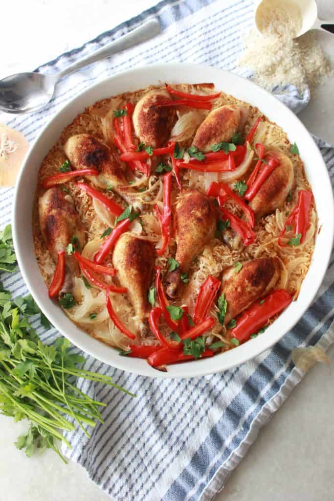 Chicken and rice cooked in one large white pan with onions and peppers on top