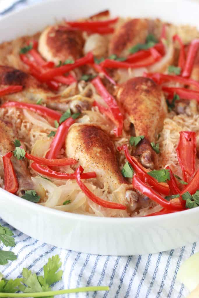Chicken and rice cooked in one large white pan with onions and peppers on top
