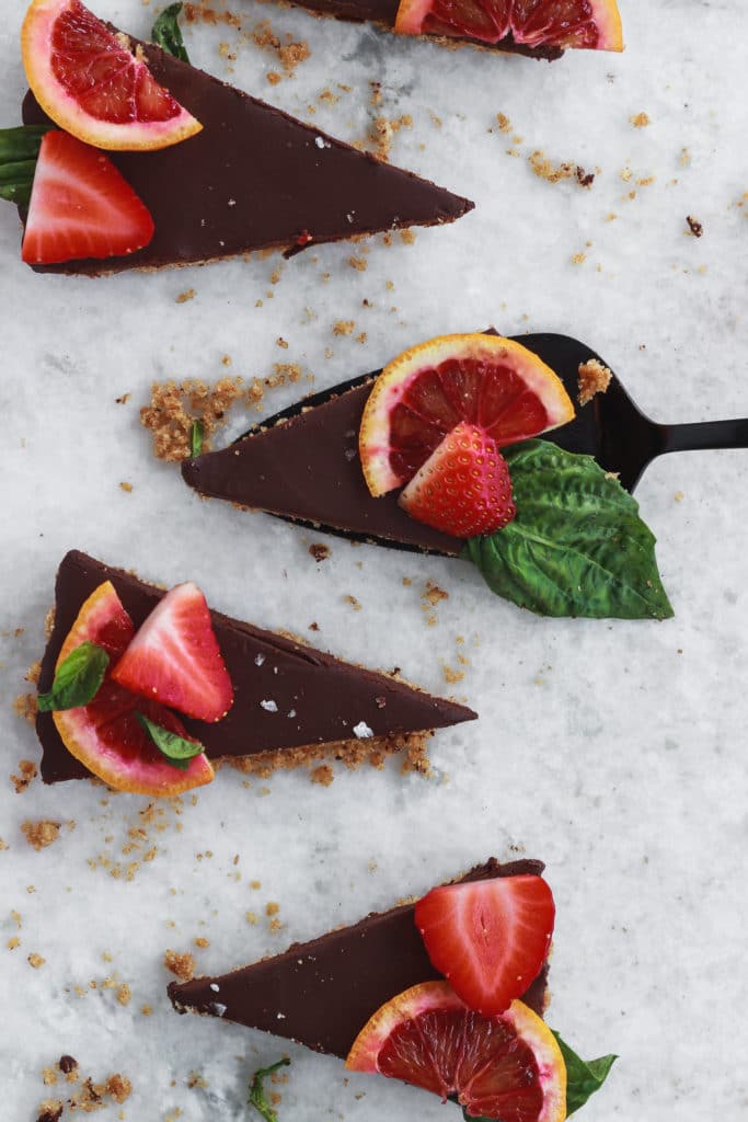 Slices of a chocolate tart topped with sliced blood oranges and strawberries