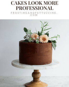 A chocolate cake on a marble and wood cake stand decorated with pink flowers