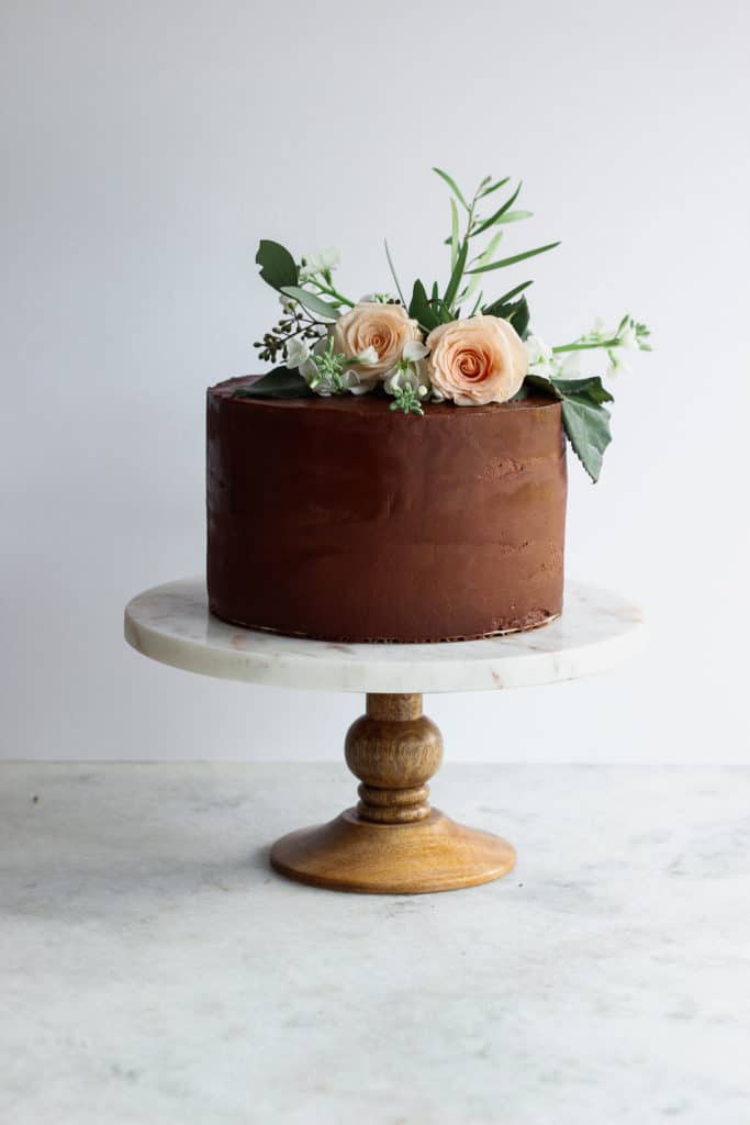 A chocolate cake with fresh flowers on a white stand, demonstrating how to decorate a cake with flowers