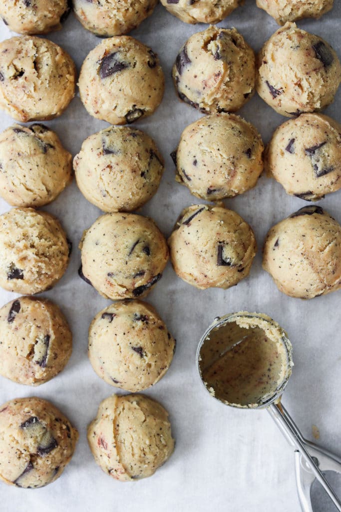 coffee cookie dough with with chocolate chunks lined up in balls on a sheet tray.