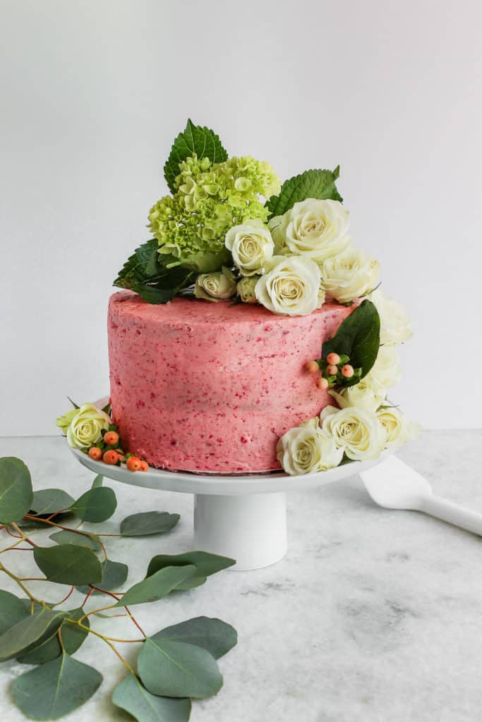 A pink cake decorated with fresh flowers with a tutorial on how to decorate a cake with flowrers