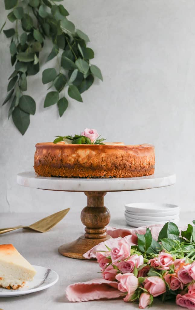 A cheesecake on a marble and wood cake stand decorated with pink flowers