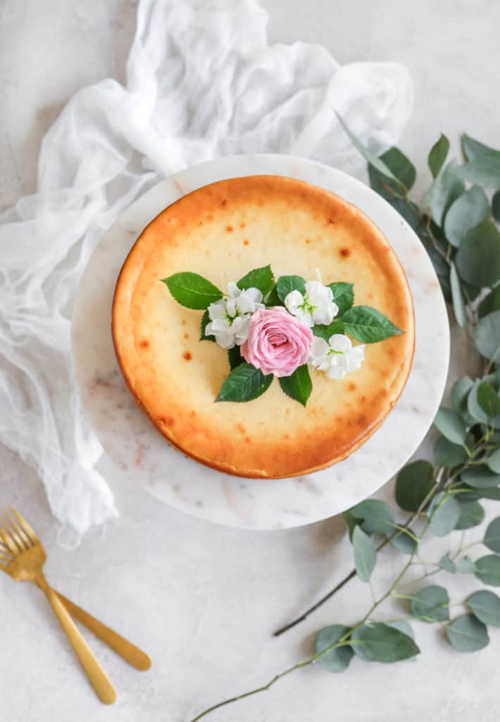 A classic cheesecake on a marble cake stand decorated with flowers