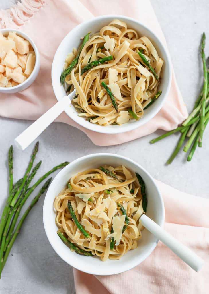 Fettuccine pasta with asparagus served in two white bowls with pink napkins