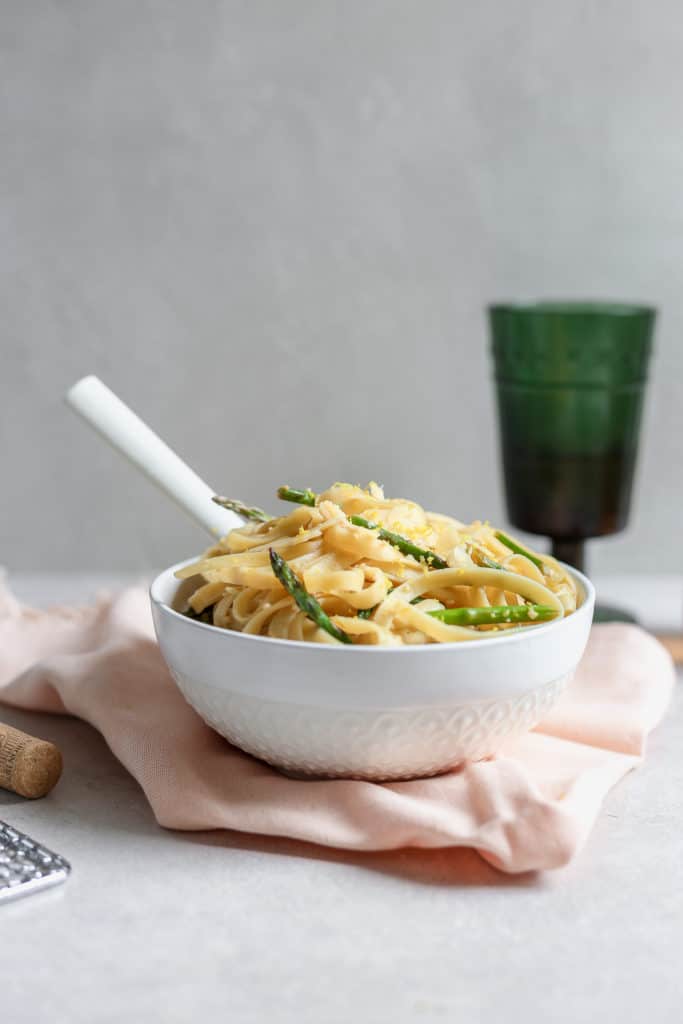 Fettuccine pasta dish with asparagus and lemon served in a white bowl over a pink napkin