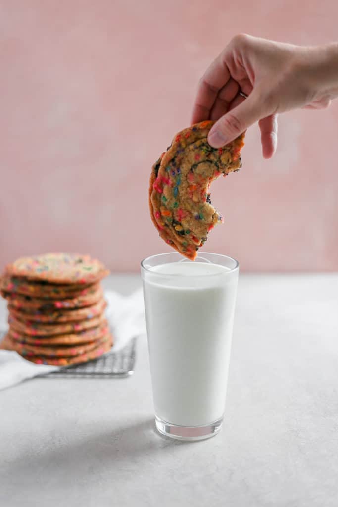 Half a cookie with sprinkles and chocolate about to be dunked into a cup of milk