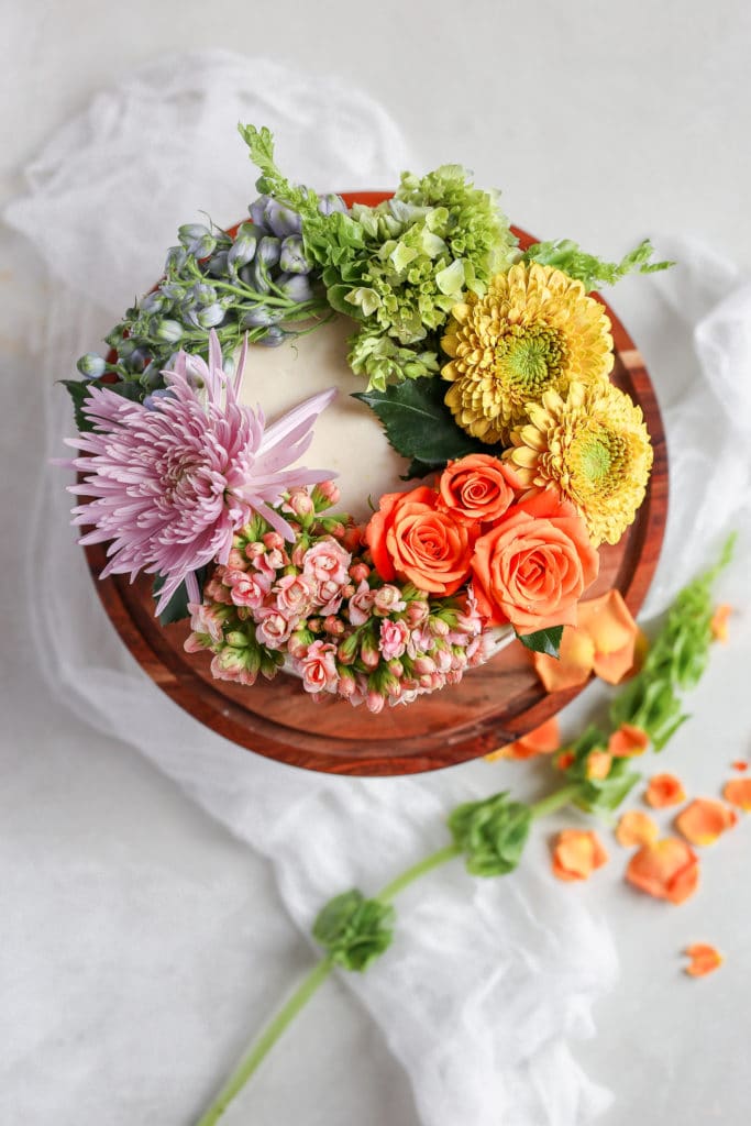 A white cake on a brown cake stand to show how to decorate a cake with flowers.