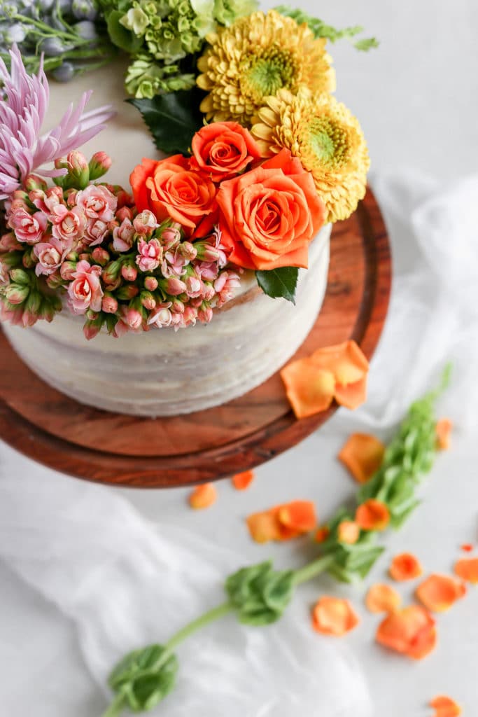 A white cake on a brown cake stand decorated with a rainbow of fresh flowers demonstrating how to decorate a cake with flowers