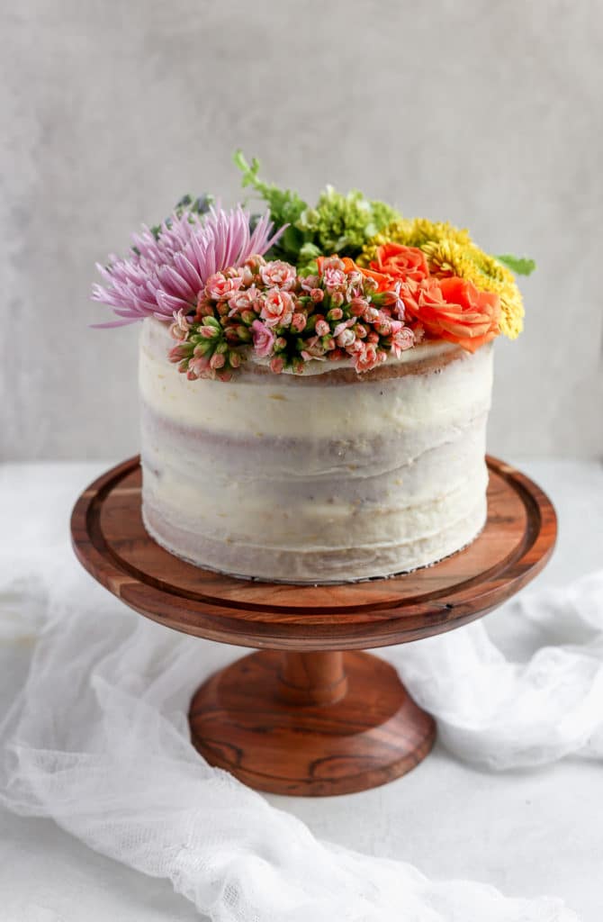 A white cake on a brown cake stand decorated with a rainbow of fresh flowers demonstrating how to decorate a cake with flowers