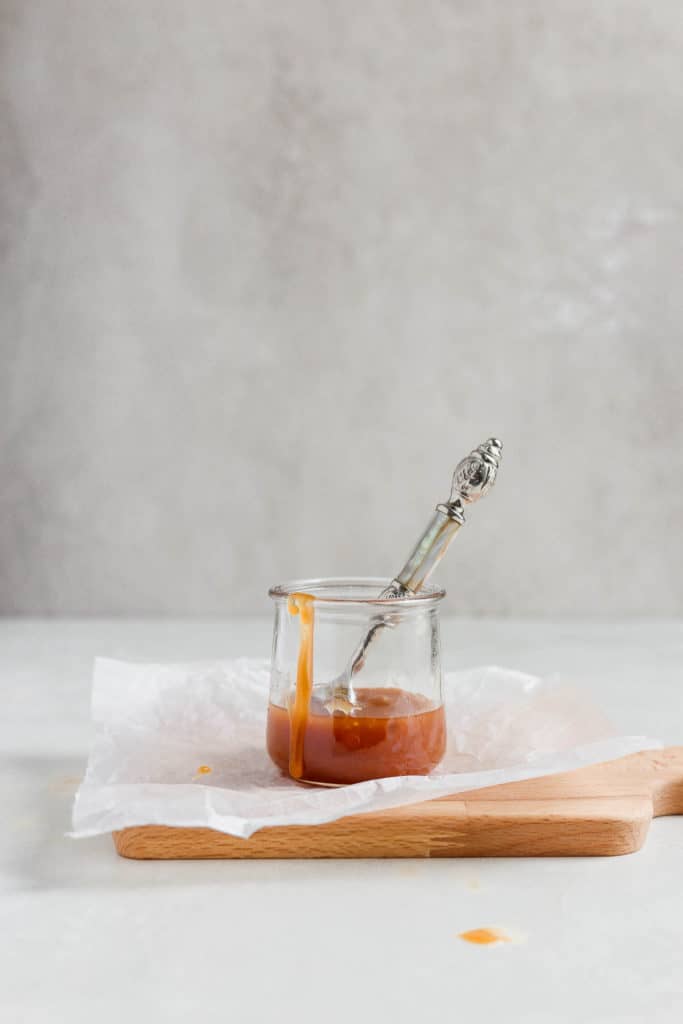 Dairy free caramel sauce styled in a jar with a pretty spoon sticking out. 