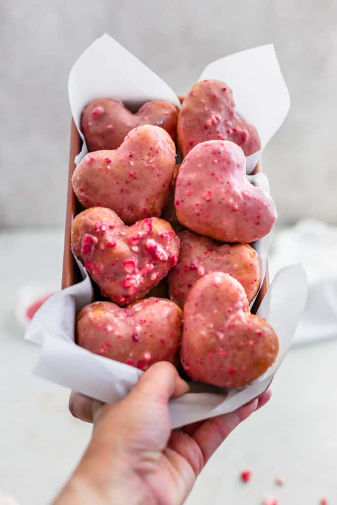 Strawberry heart donuts being held up in an orange loaf pan