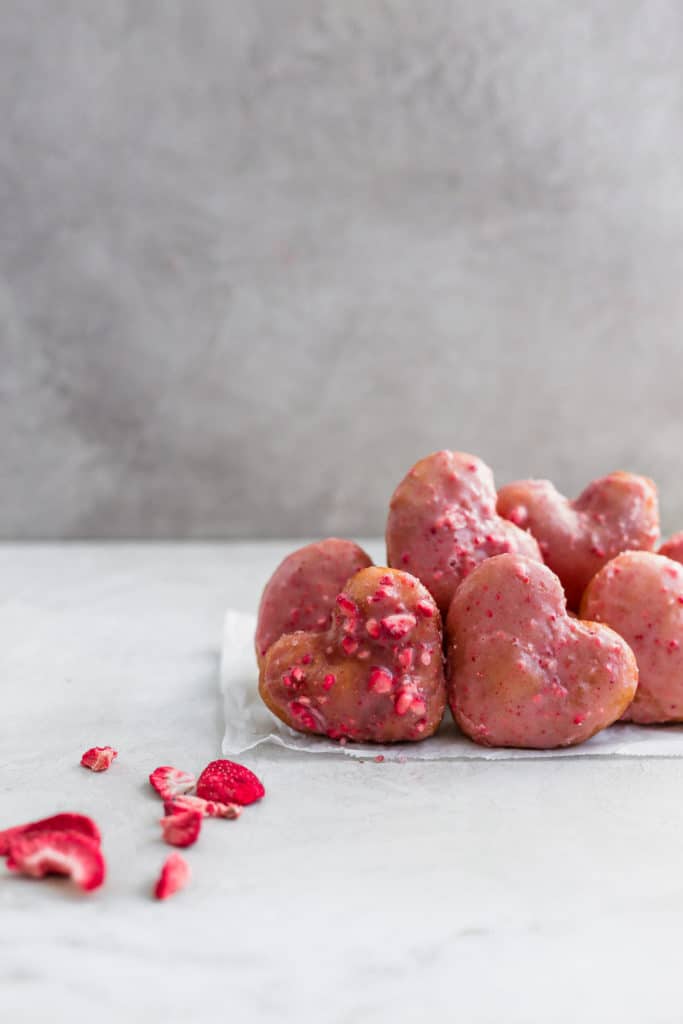 Strawberry heart donuts lined up on a gray background.