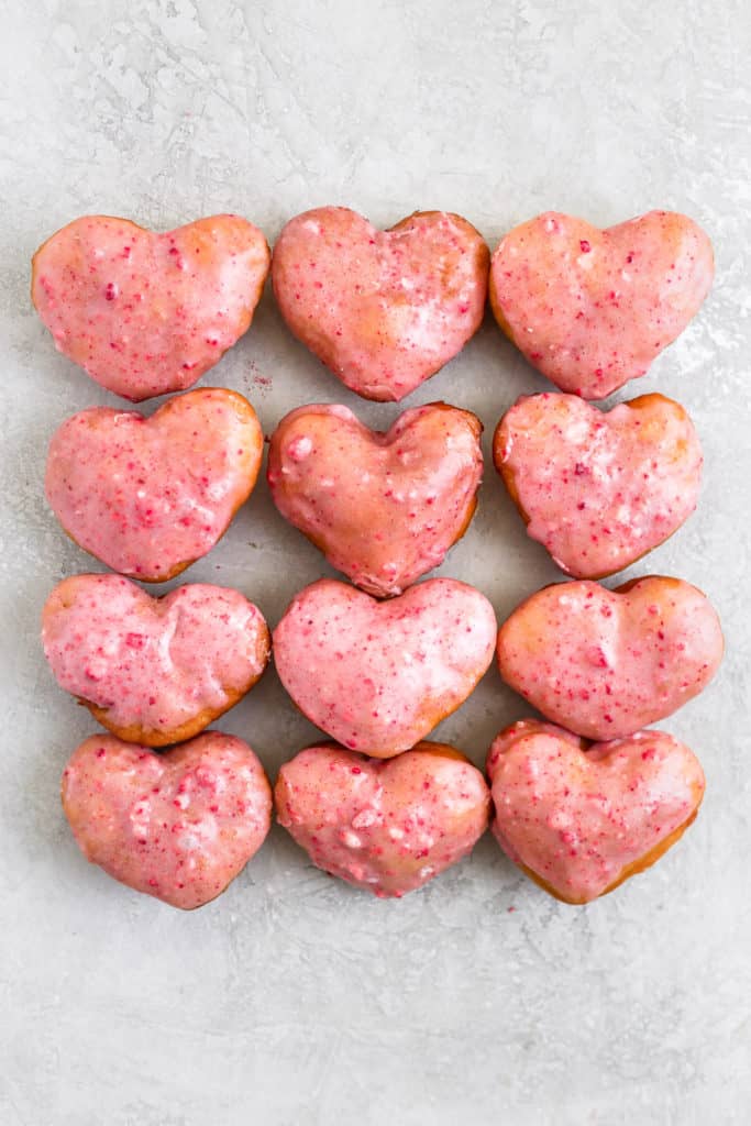 An arrangement of pink strawberry heart shaped donuts on a gray background.