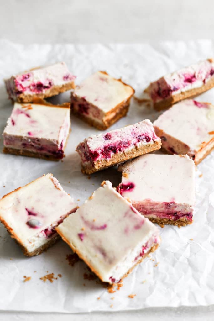 Slices of a cheesecake bar recipe with cranberry sauce styled on a white background. 