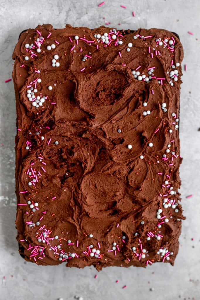 A one bowl chocolate cake with chocolate buttercream and sprinkles sheet cake on a gray background.