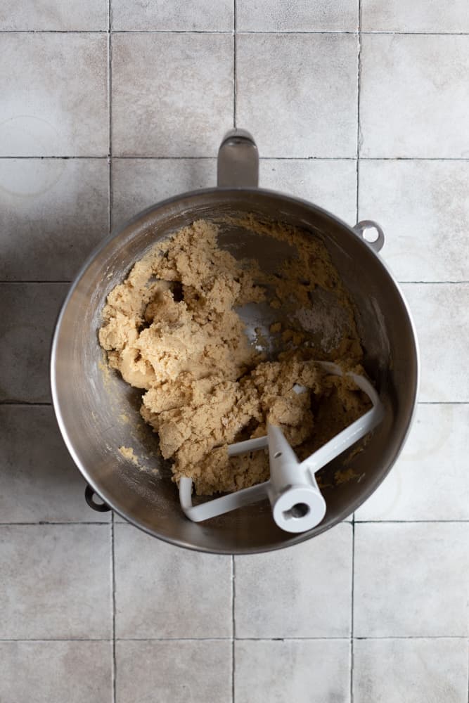 Butter, sugar, and brown sugar creamed in a stainless steel mixing bowl on a gray tiled surface