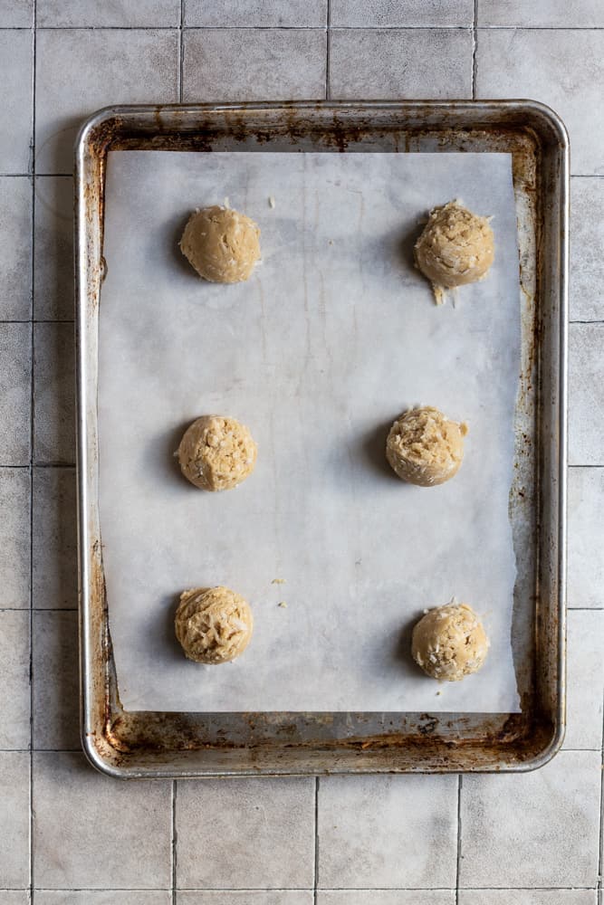 6 cookie dough balls on a parchment lined baking sheet