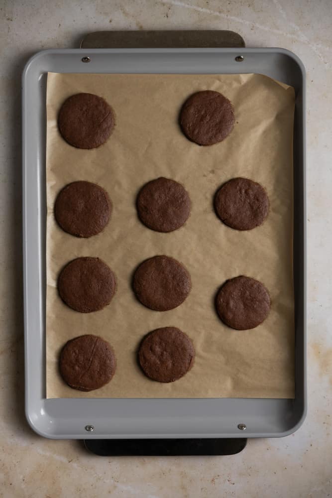 Chocolate shortbread rounds on a parchment lined baking sheet.