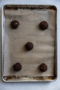 5 cookie dough balls lined up on a sheet tray.