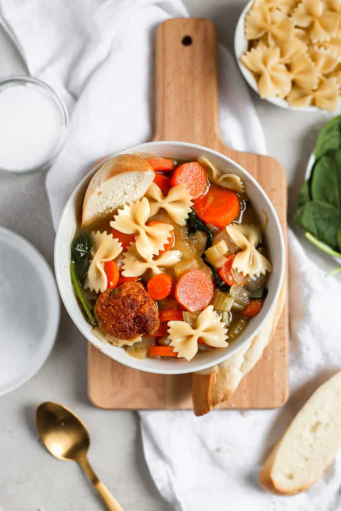 Easy Italian wedding soup with a turkey meatball in a white bowl styled on a cutting board. Frosting and Fettuccine 