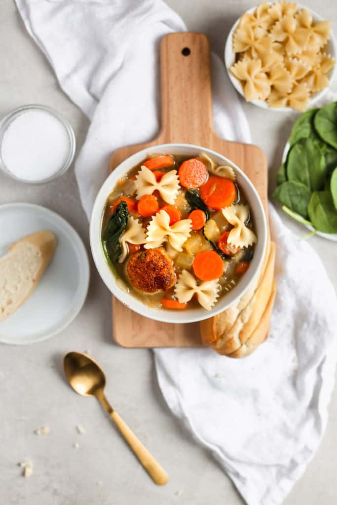 Easy Italian wedding soup with a turkey meatball in a white bowl styled on a cutting board. Frosting and Fettuccine 