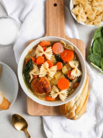 Easy Italian wedding soup with a turkey meatball in a white bowl styled on a cutting board. Frosting and Fettuccine