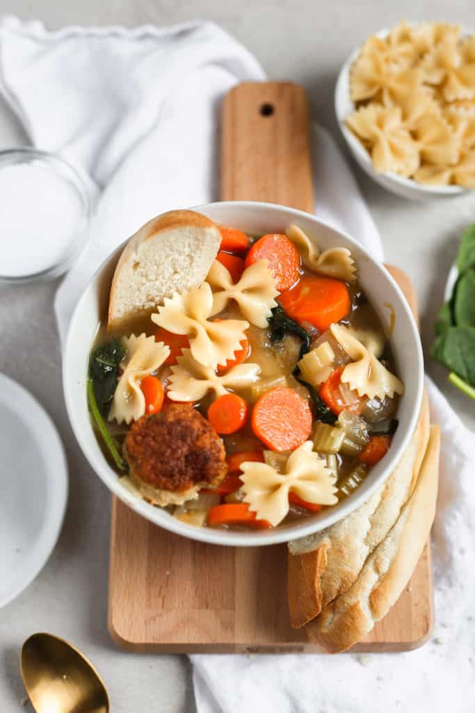 Easy Italian wedding soup with a turkey meatball in a white bowl styled on a cutting board. Frosting and Fettuccine 