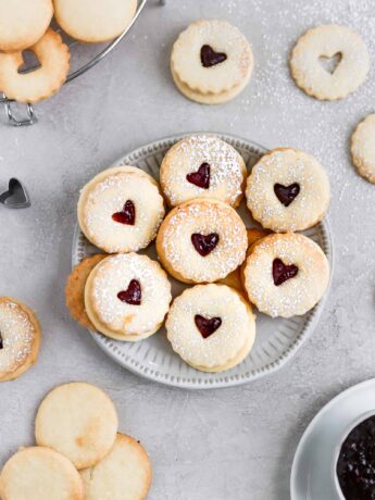 Raspberry lemon linzer cookies displayed on a small plate on a grey background.