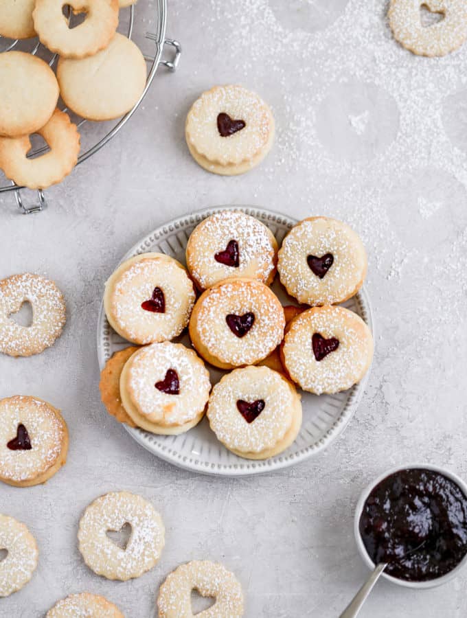 Raspberry lemon linzer cookies displayed on a small plate on a grey background.