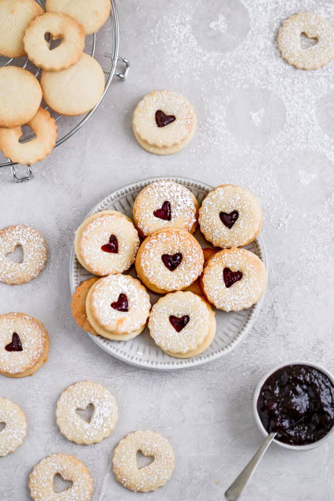 Raspberry lemon linzer cookies displayed on a small plate on a grey background. 