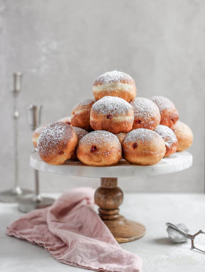 Chanukah jelly donuts arranged on a cake stand with candlestick in the background.
