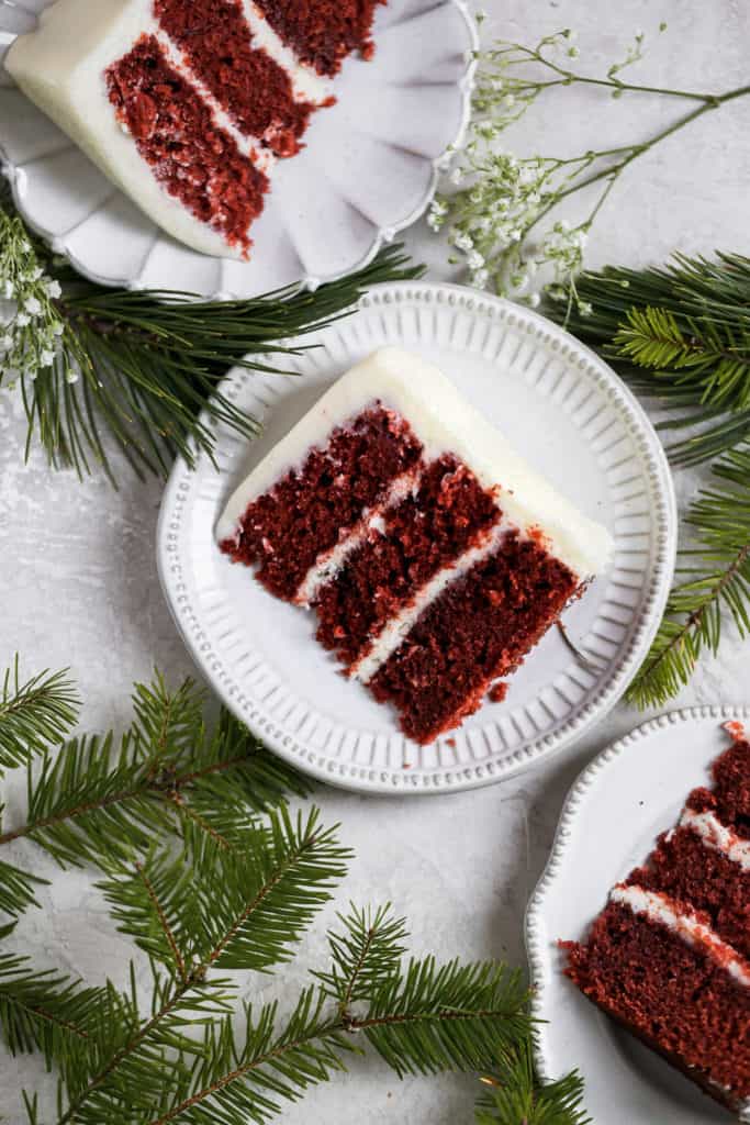 A slice of homemade red velvet cake on a small gray plate with a gold fork styled on a gray background.