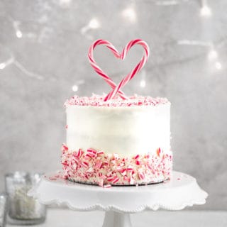 A peppermint cake on a white cake stand surrounded by fairy lights.