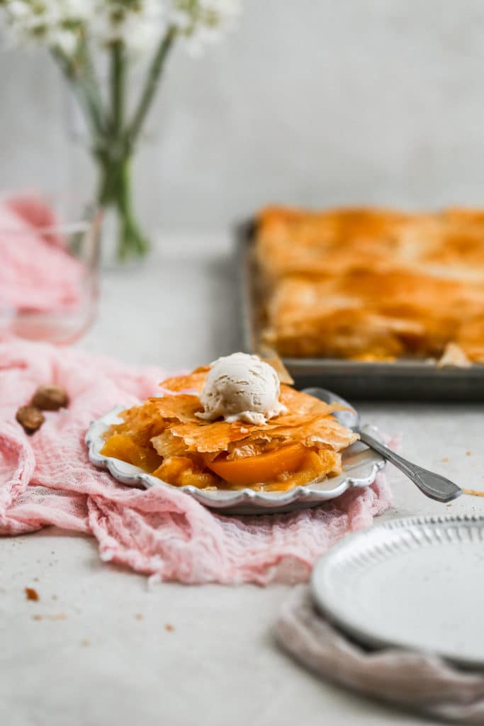 A piece of peach slab pie on a gray plate topped with ice cream.