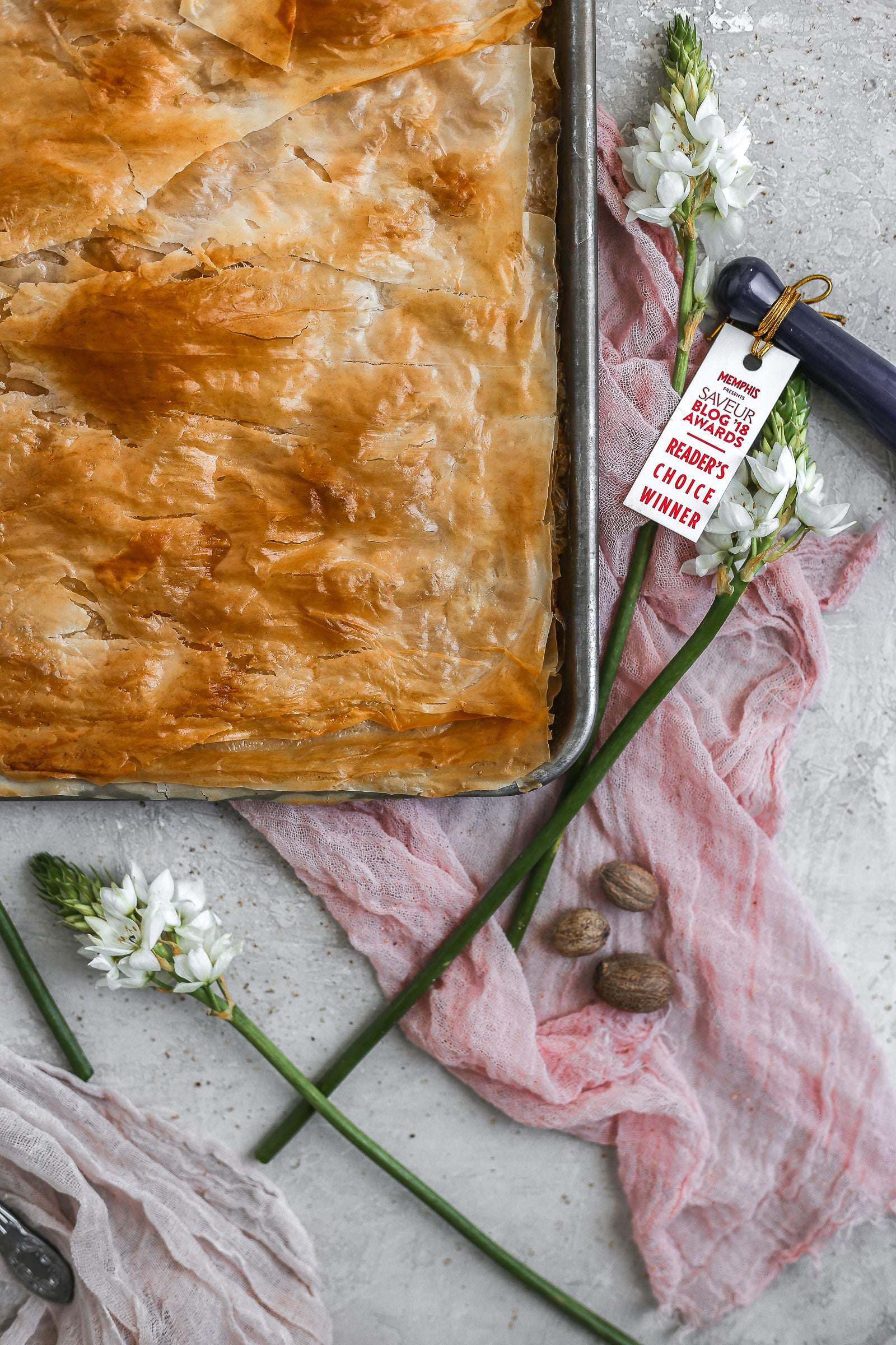 The corner of a peach slab pie in a sheet pan styled on pink cheesecloth and flowers.