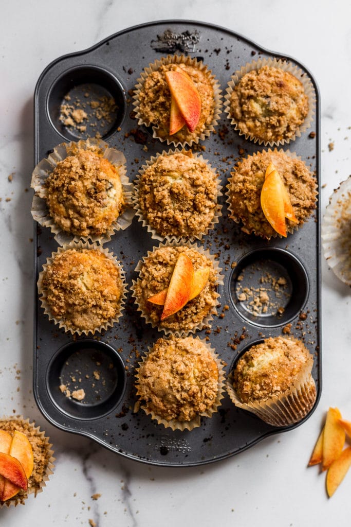 Peach muffins with crumb topping in a muffin tin.