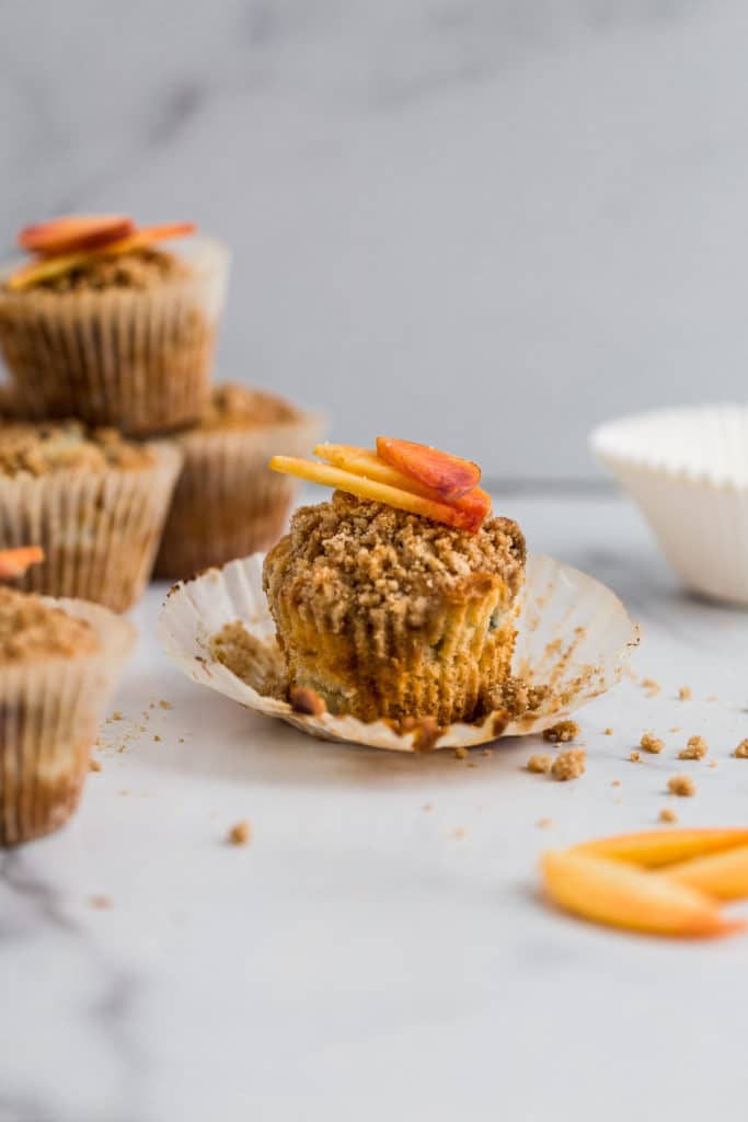 A peach muffin with crumb topping unwrapped from its liner.