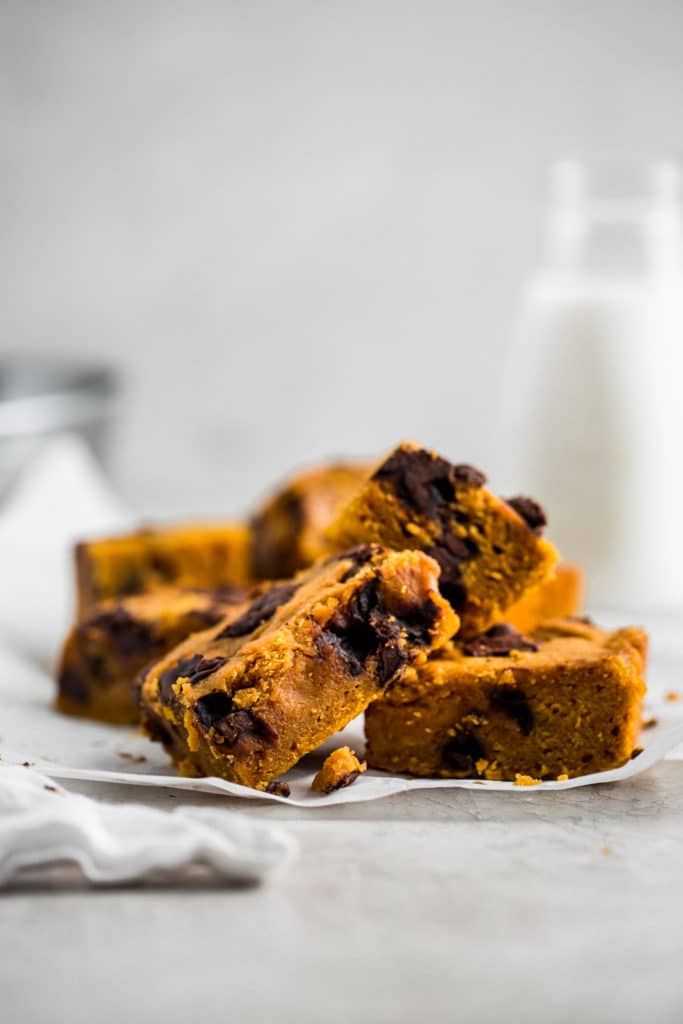 Pumpkin bars with chocolate chunks laid out on parchment paper with milk in the background