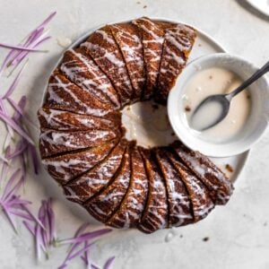 A sliced bundt cake with white glaze drizzled nex to the bowl of glaze.