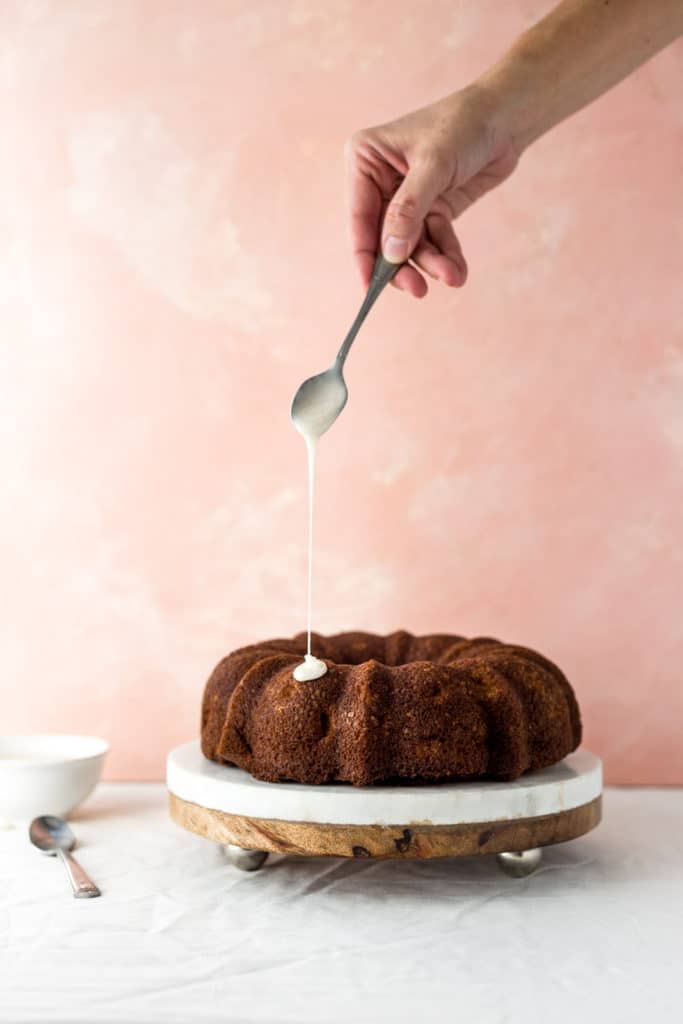 A bundt cake on a marble cake stand about to be drizzled with glaze