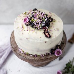 The top of a white cake with blackberries and flowers.