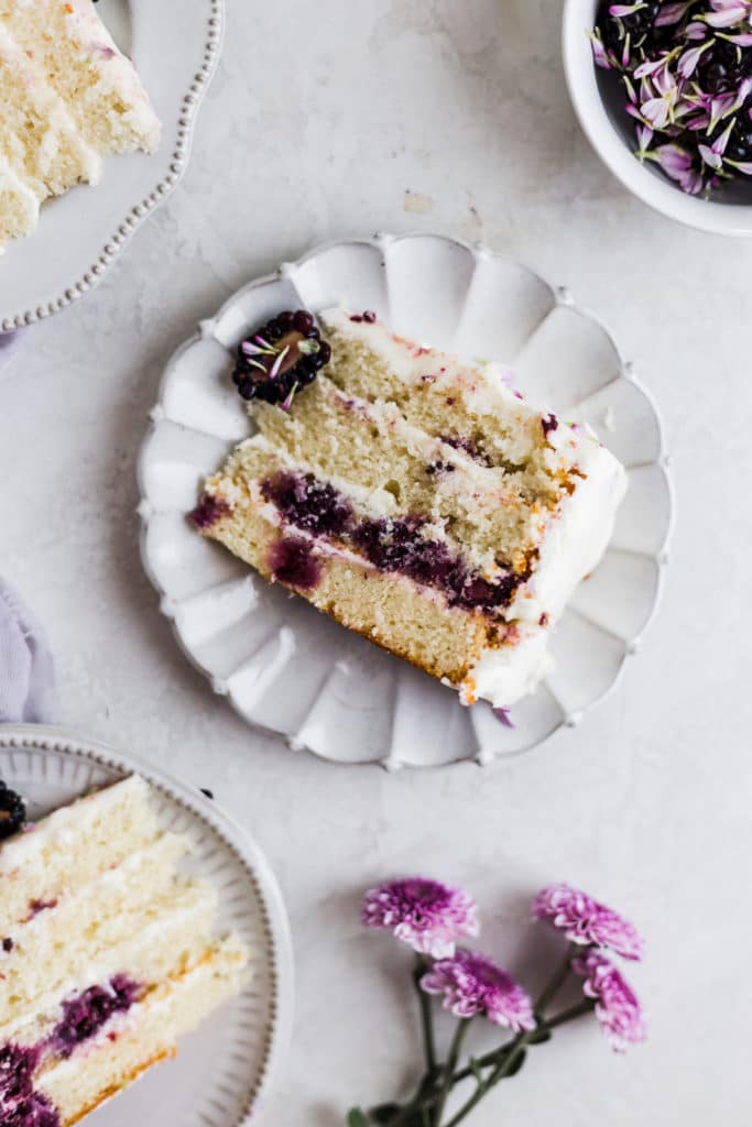 White cake with blackberries on a gray rimmed plate.
