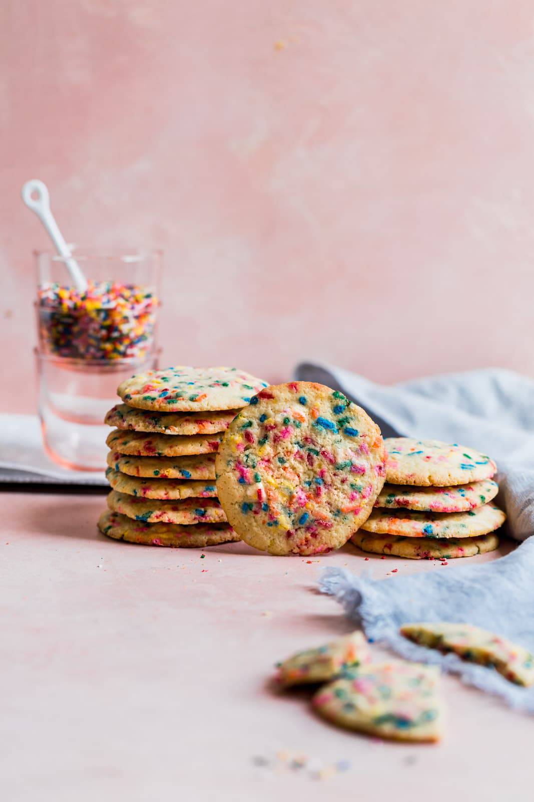cookies with sprinkles stacked together on a pink background.