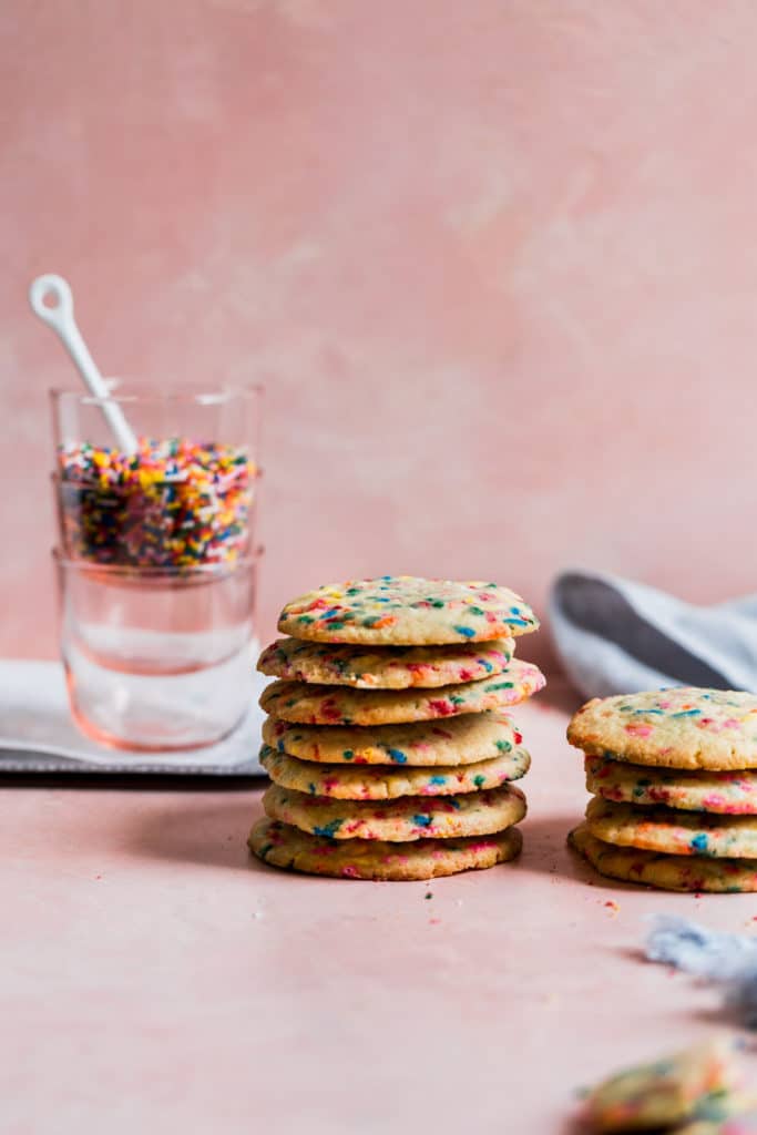 cookies with sprinkles stacked together on a pink background.